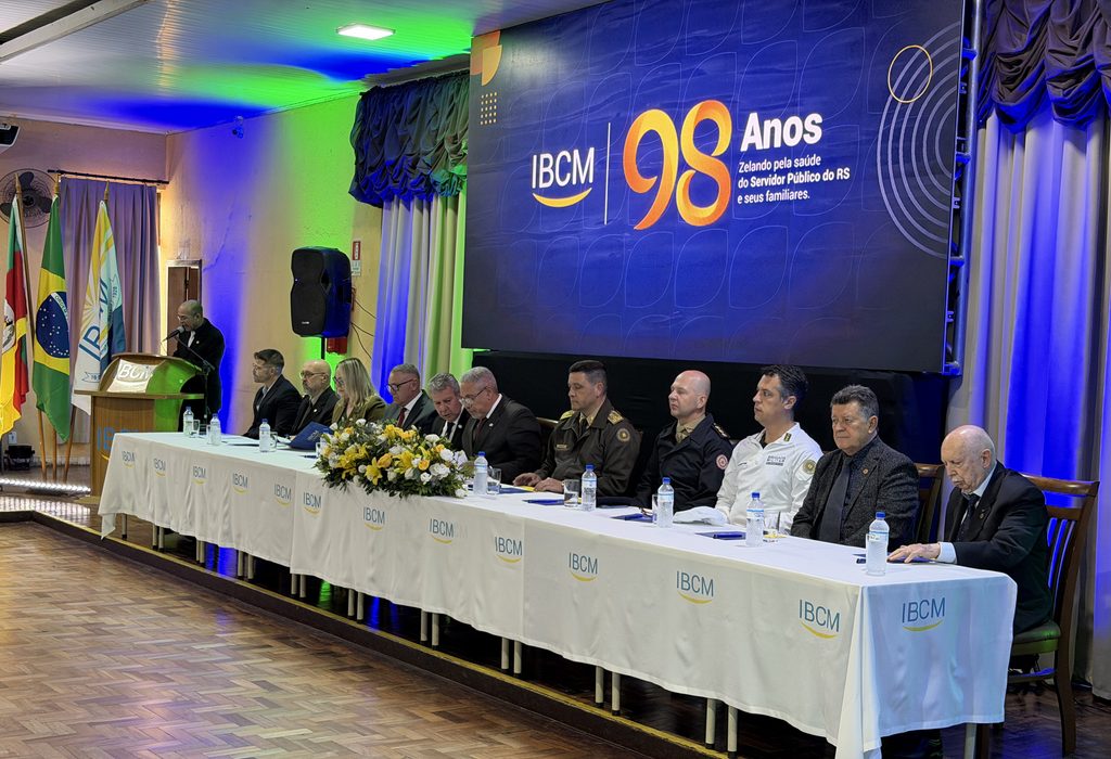 Mesa de honra de evento institucional com autoridades sentadas lado a lado em celebração aos 98 anos da IBCM. Ao fundo, um painel digital exibe a marca "IBCM 98 Anos - Zelando pela saúde do Servidor Público do RS e seus familiares"